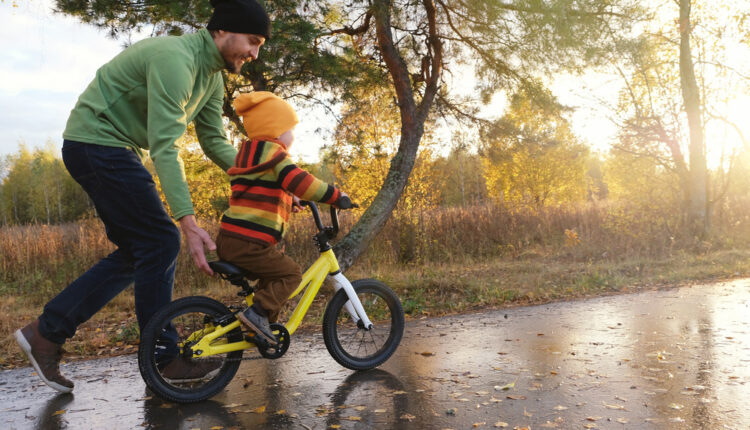 Father teaches his little child to ride bicycle in autumn park.